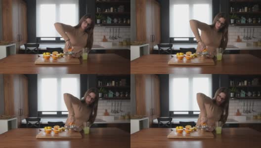 年轻的商业妇女在去工作之前，在厨房用橙子水果和柠檬制作维生素炸弹能量饮料果汁。女性健康生活理念。高清在线视频素材下载