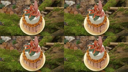 婚礼蛋糕上有两层，浅奶油和新鲜水果，在仪式前装饰好，放在森林中央的树干上，树干上覆盖着一层黑色的苔藓高清在线视频素材下载