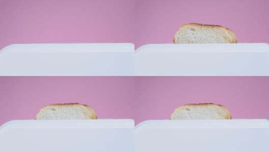 在粉红色的背景下，烤面包从白色的烤面包机里跳出来，特写高清在线视频素材下载