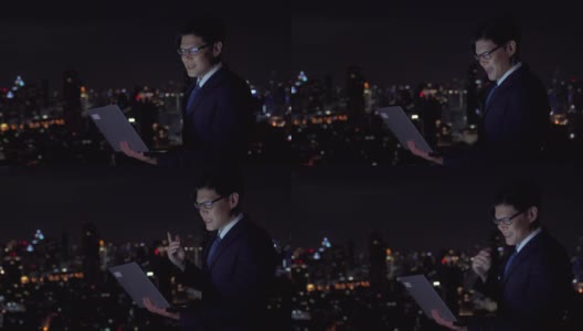 4K年轻的亚洲商人使用笔记本电脑与互联网视频会议与商业团队头脑风暴的想法，在城市的夜晚灯光背景下的办公楼成功的项目高清在线视频素材下载