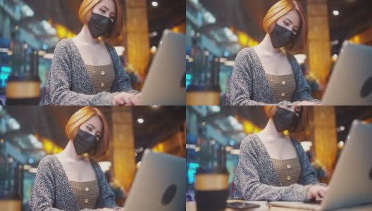 穿着休闲服装的美丽亚洲女人，戴着防护口罩，以防止病毒Covid-19健康危机的传播，在咖啡店使用笔记本电脑工作高清在线视频素材下载
