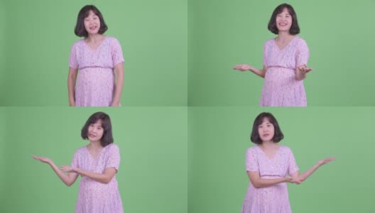工作室拍摄的漂亮的亚洲孕妇显示拷贝空间和做对比的绿色工作室背景高清在线视频素材下载