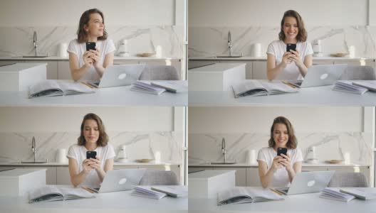 快乐的女人坐在桌子旁边，拿着笔记本电脑和日记，用智能手机写信息高清在线视频素材下载