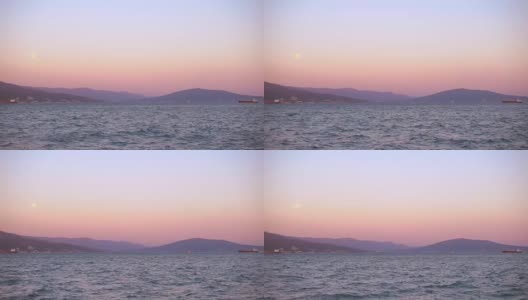 美丽的夕阳和月亮照耀着港口城市，远处有船只。高清在线视频素材下载