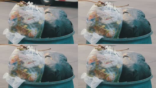 在汽车和摩托车行驶的繁忙街道上，塞满塑料袋、剩饭剩菜和其他垃圾的垃圾桶高清在线视频素材下载