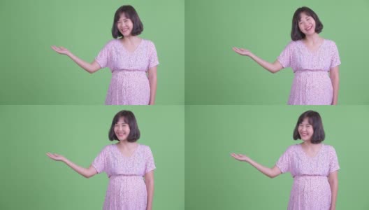 摄影棚拍摄了美丽的亚洲孕妇微笑和显示拷贝空间在绿色的摄影棚背景高清在线视频素材下载