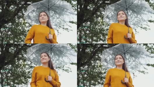 在阴雨寒冷的天气里，一个穿着芥末色毛衣的女人站在一把透明的伞下高清在线视频素材下载
