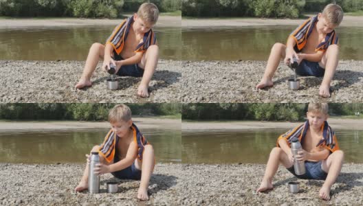 一个十几岁的男生赤裸着身体，脖子上围着一条毛巾，坐在河边，从一个钢瓶里给自己倒热茶。乡村的夏日阳光灿烂。高清在线视频素材下载