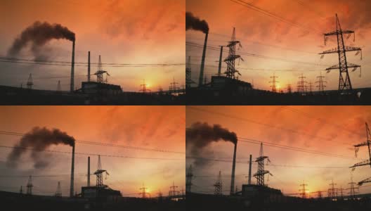 红色夕阳下，有害工厂附近的电塔。黑烟从工业管道释放到空气中。输电线路。污染环境。摄像头向下运动。高清在线视频素材下载