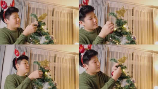 快乐的亚洲男孩戴着驯鹿发带，晚上在家装饰圣诞树，庆祝节日的概念。高清在线视频素材下载