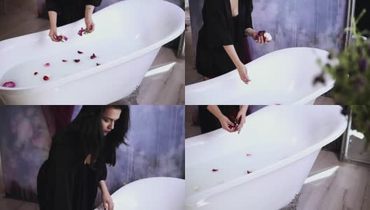 年轻迷人的女子在黑色浴衣扔花到浴缸装满牛奶，准备洗个热水澡。Slowmotion拍摄高清在线视频素材下载