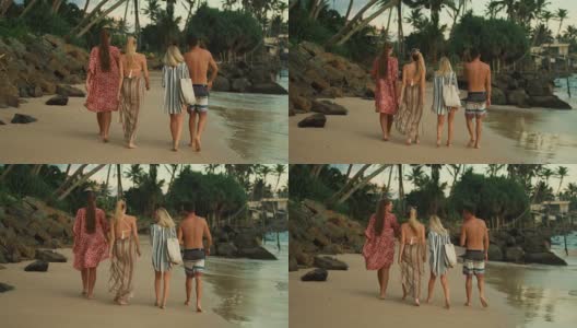 三个漂亮的女孩和一个英俊的男人在海滩上散步。甘美的绿色森林与棕榈树在他们之前。高清在线视频素材下载