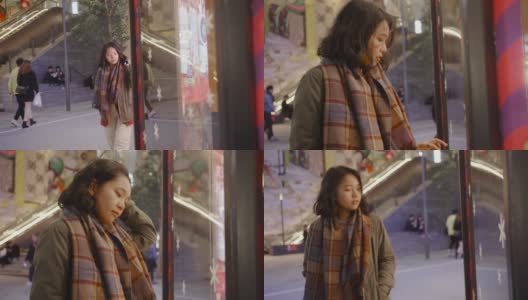 亚洲女孩妇女站在商店的窗户外，在一个寒冷的夜晚在城市里寻找圣诞礼物，她穿着暖和的衣服。高清在线视频素材下载