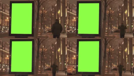 人行道上的绿色屏幕广告牌，靠近繁忙的街道，供人们行走。汽车在晚上行驶。高清在线视频素材下载