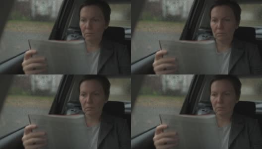 女商人在雨中坐在汽车后座读商业报告高清在线视频素材下载