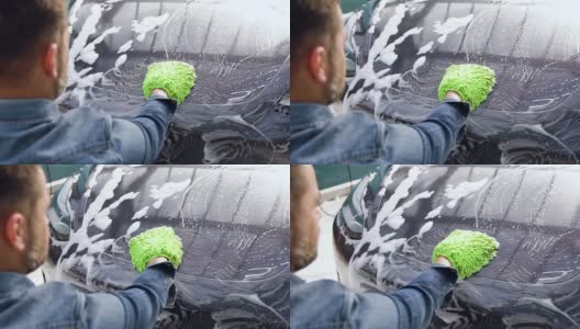 年轻英俊的大胡子男子在户外洗车时用泡沫海绵洗自己的车高清在线视频素材下载
