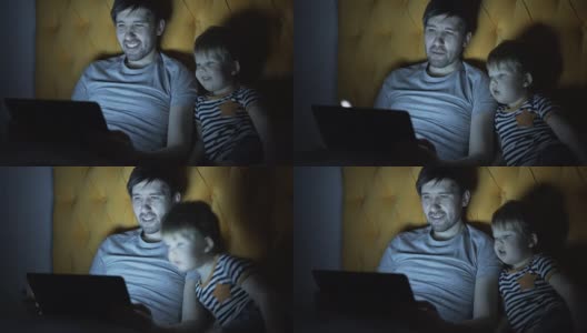 年轻的父亲和他的小儿子晚上躺在床上看卡通电影高清在线视频素材下载
