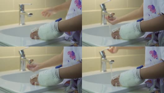 当生病的女孩在医院浴室的洗脸盆里用流动的水洗手时，靠近她包扎的手高清在线视频素材下载