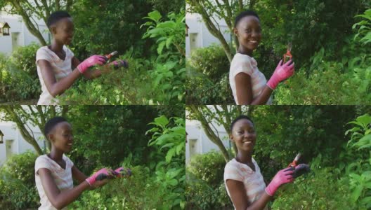 非洲裔美国妇女修剪植物在阳光灿烂的花园对着镜头微笑高清在线视频素材下载