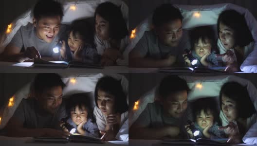 睡觉的时候，小女孩盖着毯子和爸爸妈妈一起看书高清在线视频素材下载