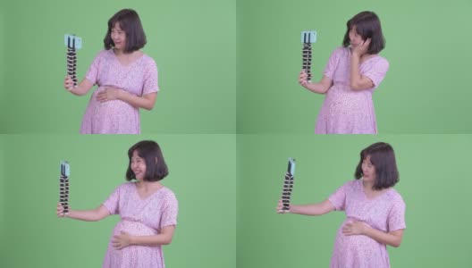 摄影棚拍摄美丽的怀孕亚洲妇女与手机视频在绿色的摄影棚背景高清在线视频素材下载
