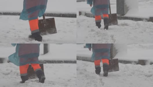 冬天。下雪的时候，一个工人穿着工作服拿着铲子在清理积雪。冬天在这个城市的街道上倒塌了。腿部特写高清在线视频素材下载