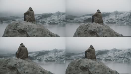 后视图的年轻游客坐在岩石上，看着冰川泻湖。独自探索冰岛的人高清在线视频素材下载