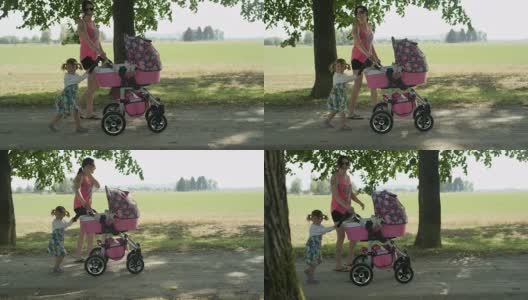 拷贝空间:微笑的女孩推着她的妹妹在婴儿车与母亲散步高清在线视频素材下载