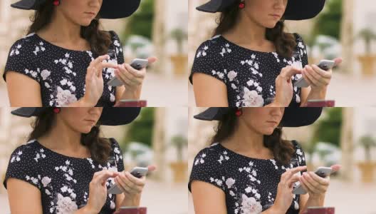 戴帽美女坐在街边咖啡馆，滚动手机应用高清在线视频素材下载