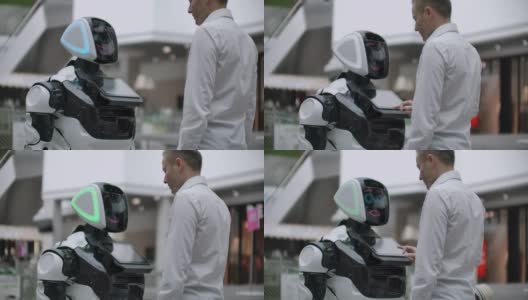 一名身穿衬衫的男子与一个白色机器人交流，机器人问问题，并用手指按屏幕。高清在线视频素材下载
