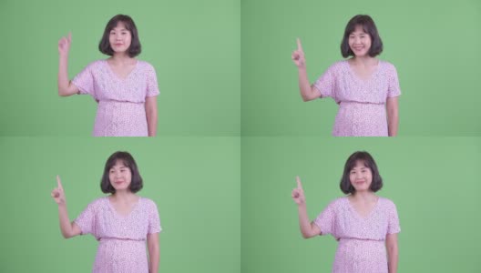 工作室拍摄的美丽的亚洲孕妇微笑和手指在复制空间对绿色的工作室背景高清在线视频素材下载